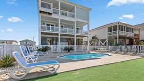 A two-story building with a pool and lounge chairs. - Discover Oak Island Nest Egg: a spacious 5-bedroom retreat with ocean views and private pool. (Oak Island)