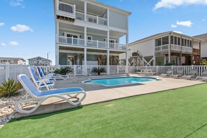 A two-story building with a pool and lounge chairs. - Discover Oak Island Nest Egg: a spacious 5-bedroom retreat with ocean views and private pool. (Oak Island)