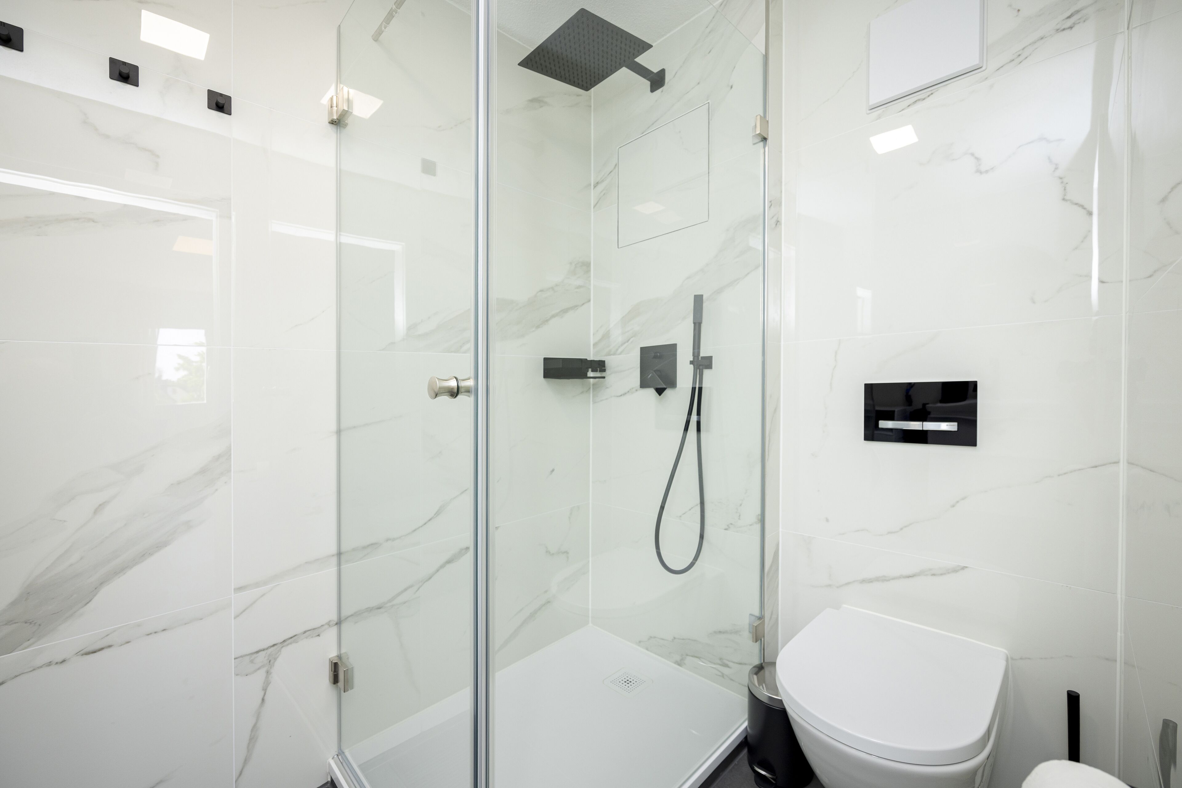 Ein modernes Badezimmer mit einer gläsernen Duschkabine, einer weißen Toilette und Marmorwänden.