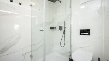Ein modernes Badezimmer mit einer gläsernen Duschkabine, einer weißen Toilette und Marmorwänden.