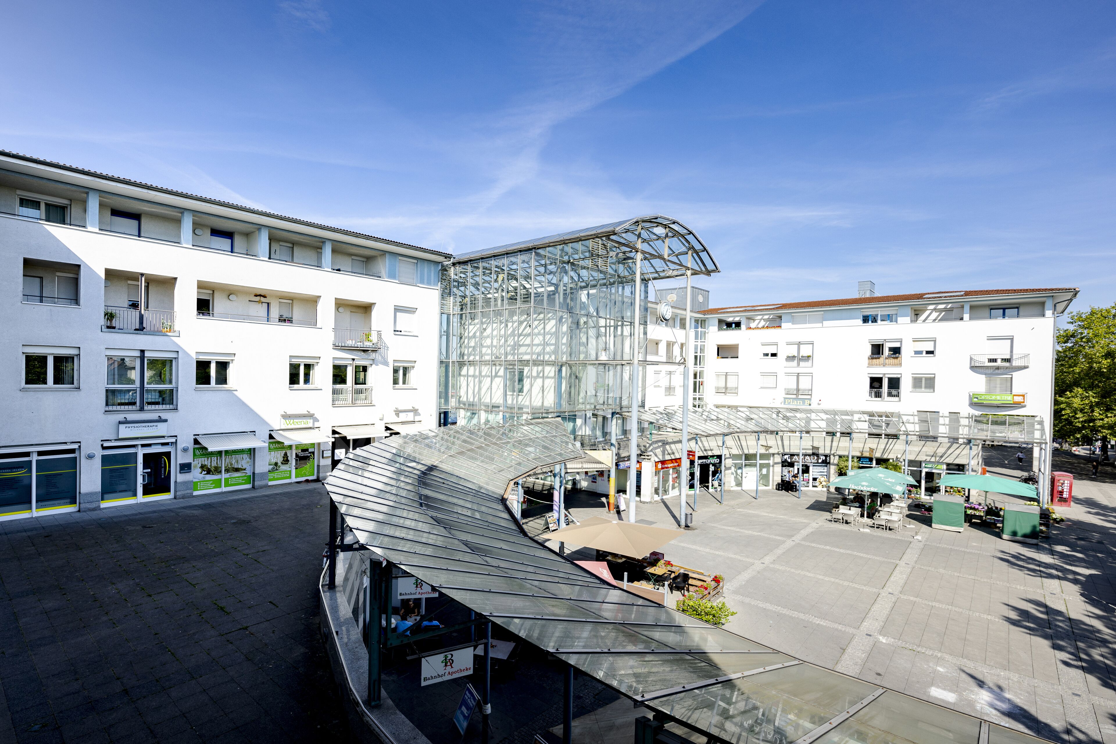 A modern building with a glass atrium, multiple floors, and a covered outdoor seating area.
