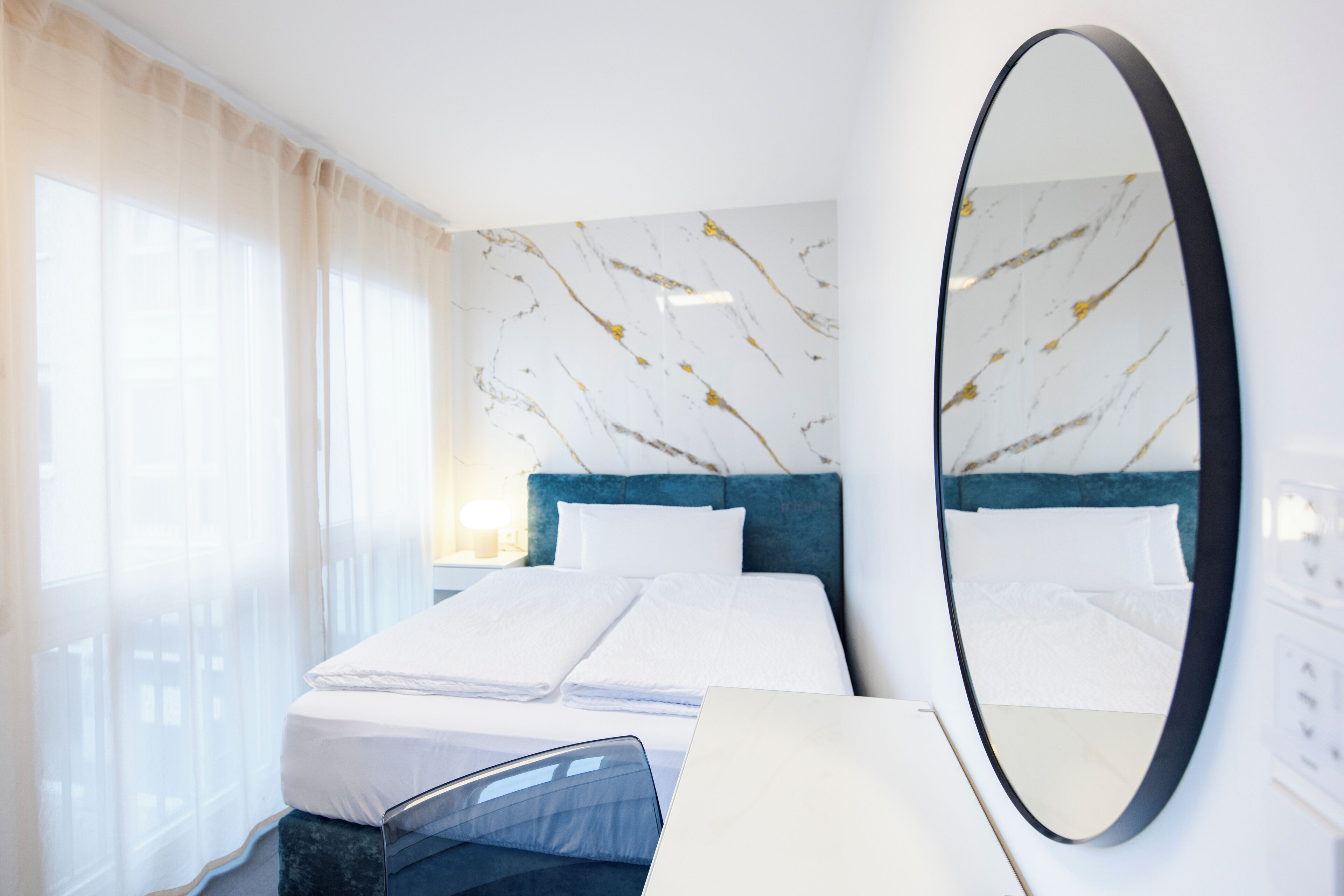 Habitació d'hotel moderna amb un llit ben arrenjat, un mirall gran i una paret amb disseny de marbre.