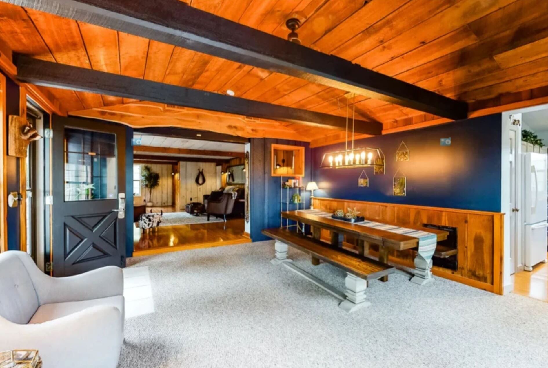 Um quarto amplo com teto de madeira, uma mesa de jantar com cadeiras e um espaço de estar com sofá branco.