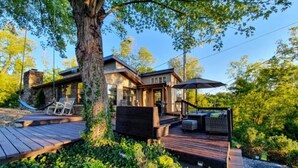 Een modern huis met een terras, buitenmeubels en een grote boom ervoor.