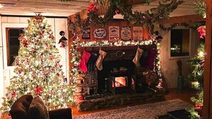 Een gezellige kamer met een versierde kerstboom, een open haard met sokken en ruwe houten wanden.