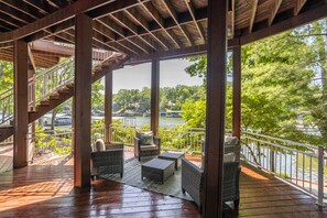 A covered outdoor deck with wicker furniture, a staircase, and a view of a lake with boats. - Cove Front, Kayak, Pedal Boat, and Nearby Restos (Rocky Mount)
