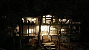 Una casa de varios niveles con una escalera que conduce al piso superior, rodeada de árboles y un exterior bien iluminado.