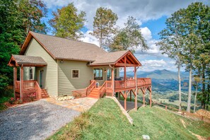 A two-story house with a wooden deck and a stone pathway leading to the entrance. - Unbelievable Views, Hot Tub, Fire Pit, Fire Table, Indoor Fireplace (Waynesville)