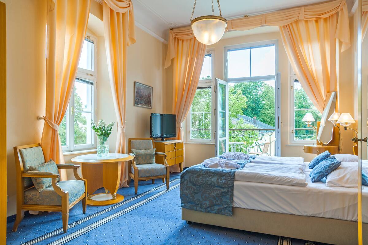 A hotel room with a bed, a television, a chair, a small table, and a window with curtains.