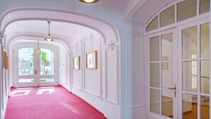 A hallway with white walls, a red carpet, and a large arched doorway leading to a room with a large window. - Tři Lilie (Frantiskovy Lazne)