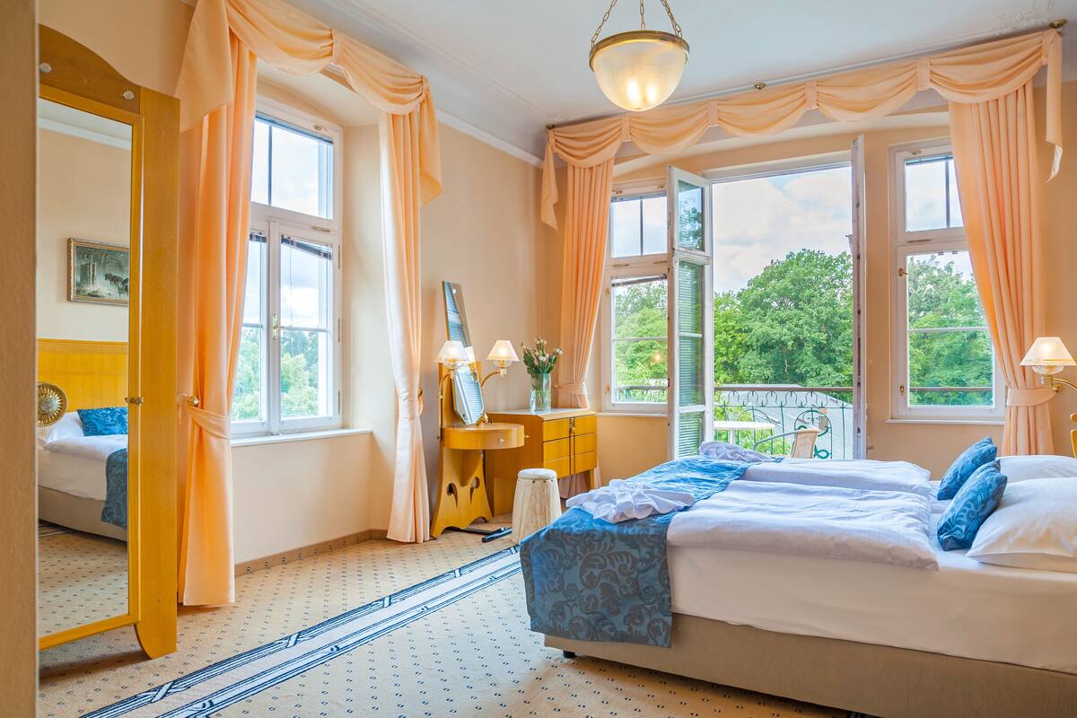 A bedroom with a large bed, a vanity, and a window with a view of greenery.