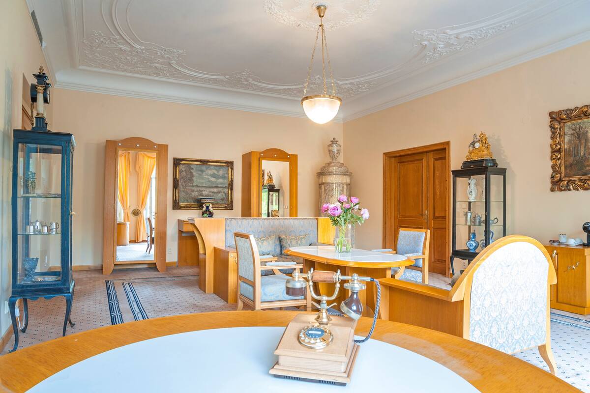 A room with a round table, a vintage telephone, a blue cabinet, and a wooden cabinet with a painting.