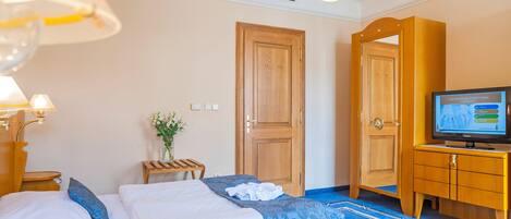 Una habitación de hotel con cama, televisión, armario de madera y una mesita con un jarrón de flores.