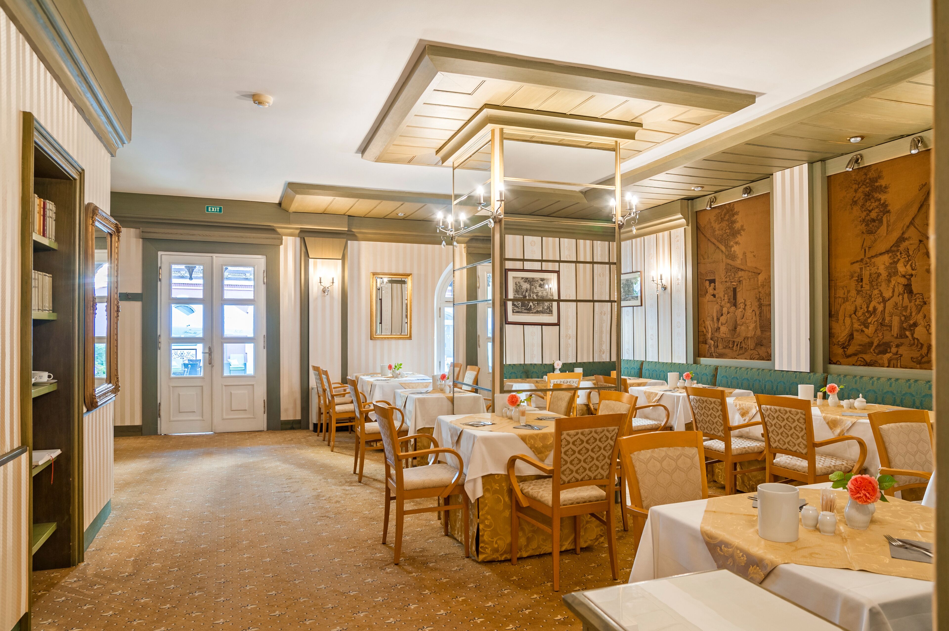 A dining area with tables set for service, wooden chairs, and a high ceiling with exposed beams.