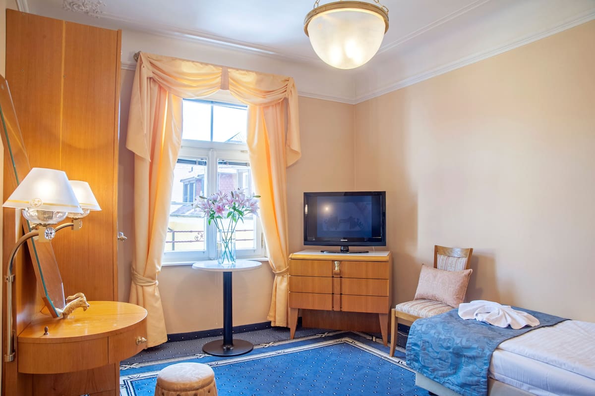 A hotel room with a bed, a TV, a small table with a vase of flowers, a lamp, and a wardrobe.