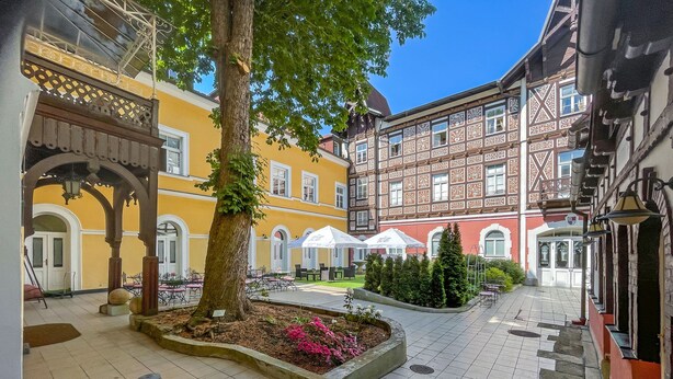 A courtyard with a tree, outdoor seating, and a building with intricate window patterns. - Tři Lilie (Frantiskovy Lazne)