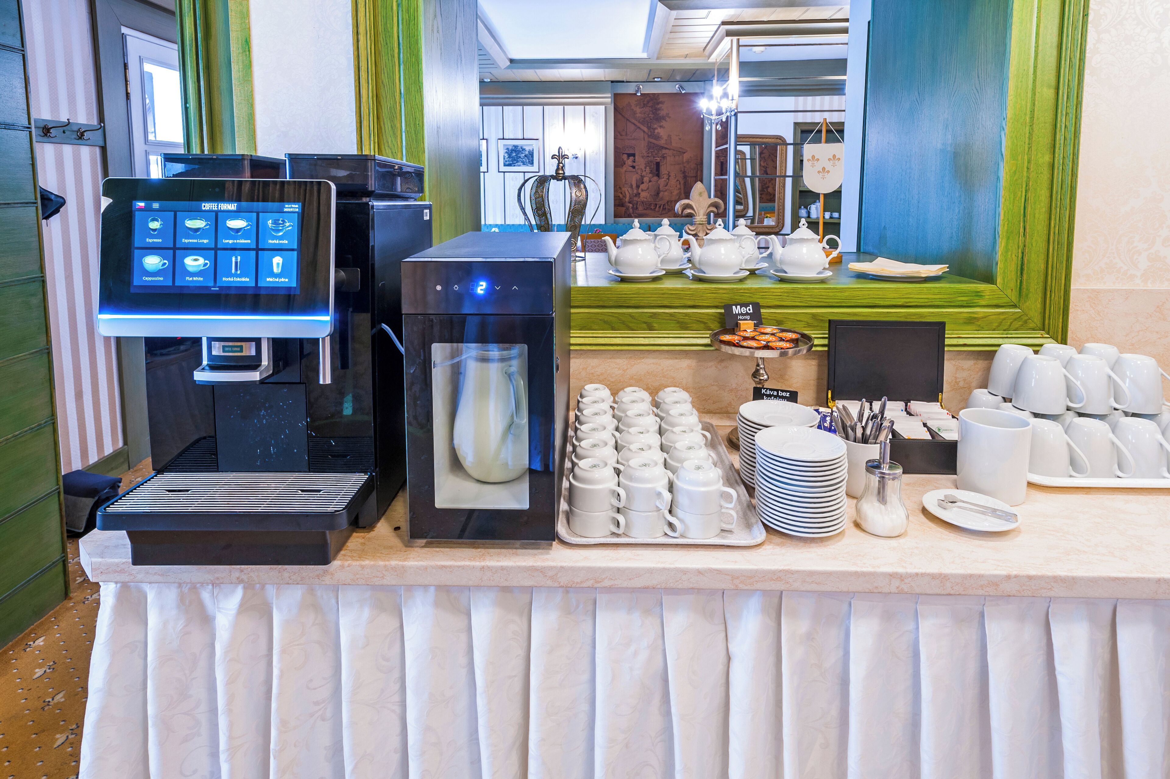 A coffee station with a coffee machine, tea pots, and a variety of cups and saucers.