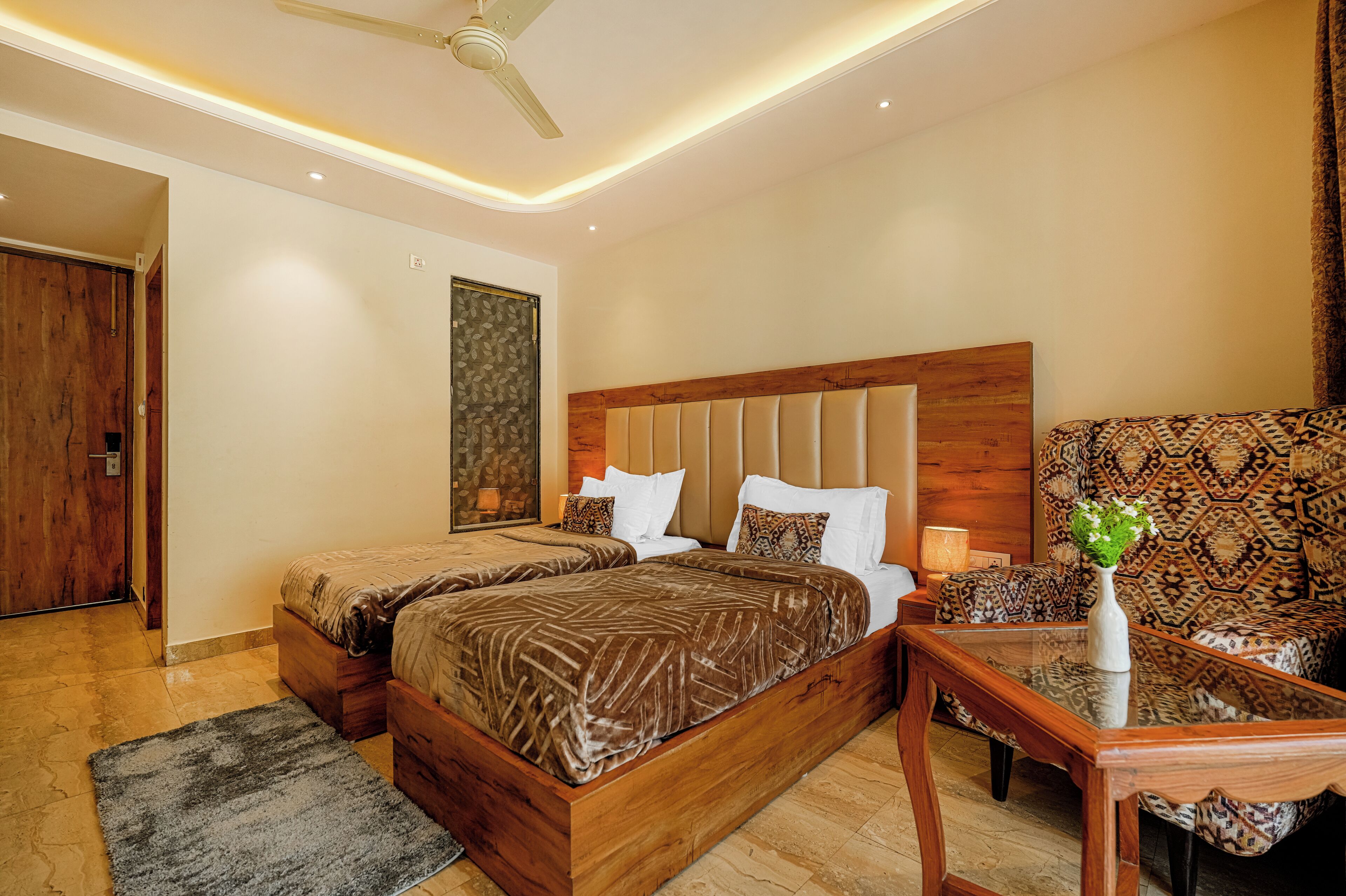 A modern bedroom with a large bed, a wooden headboard, a patterned sofa, and a small table with a vase.