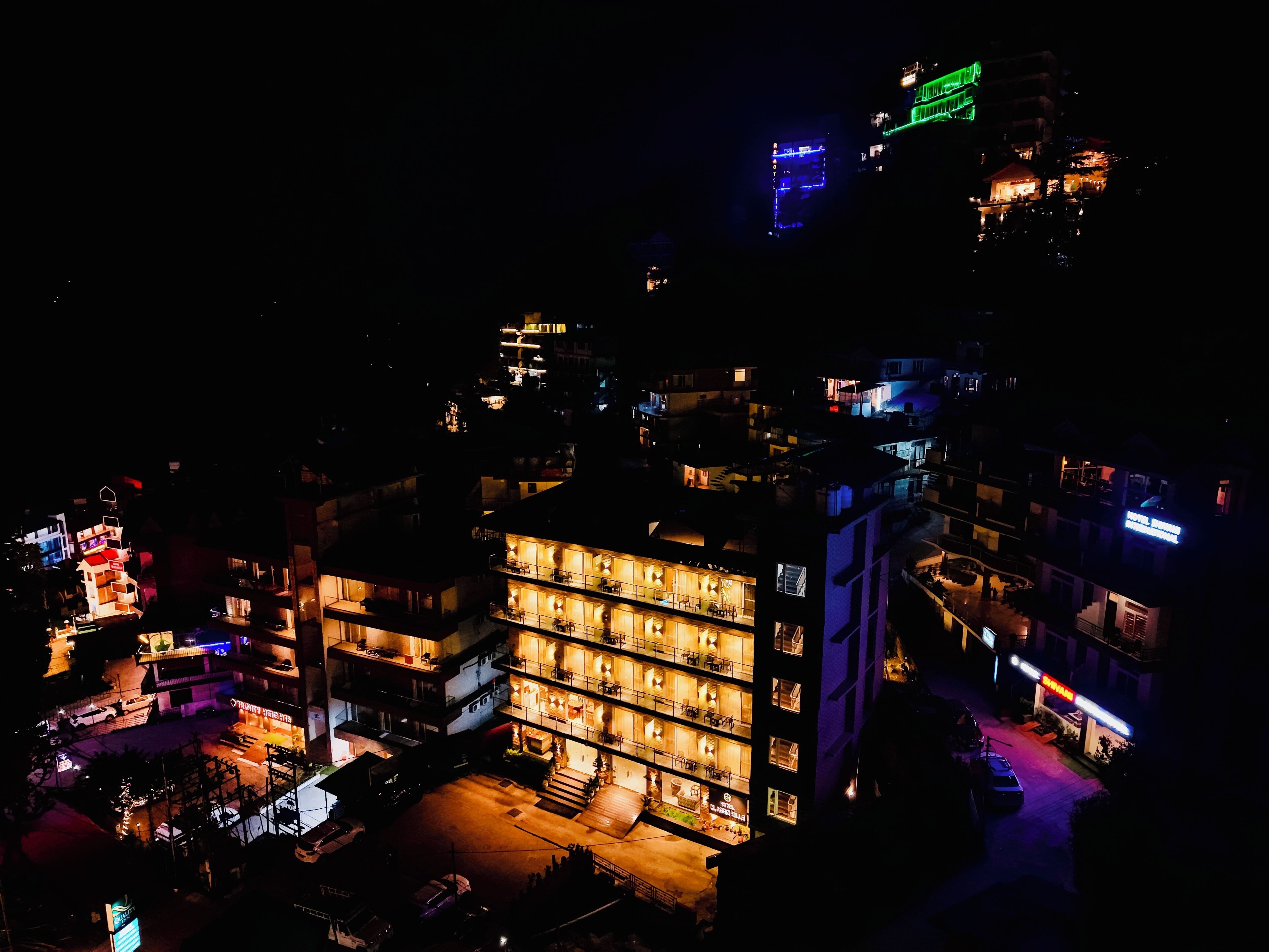 Een hotel met meerdere verdiepingen, een centrale binnenplaats, diverse balkons en een goed verlichte gevel.