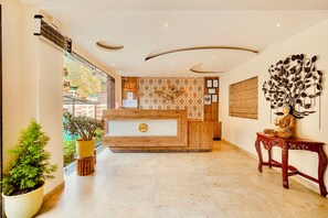 A reception area with a wooden reception desk, a wall-mounted clock, and a decorative tree sculpture. - Hotel Classic Hills (Dharamshala)