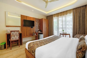 Una habitación de hotel con una cama grande, un escritorio, un televisor y un ventilador de techo.