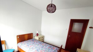 Quarto pequeno e simples com uma cama, uma cadeira, uma mesa de cabeceira e uma porta.