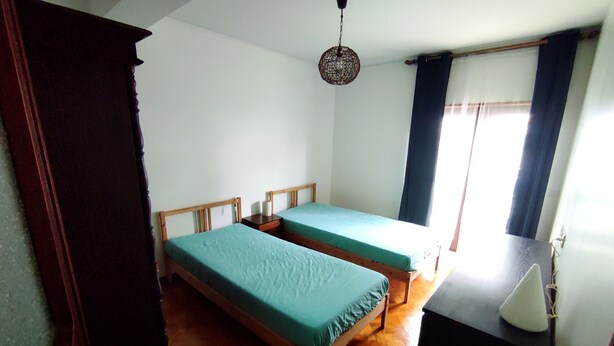 Quarto com duas camas de madeira, penteadeira de madeira, luminária pendente e janela com cortinas.