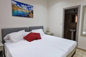 Relax in a serene space with a large bed, a coastal painting, and a bathroom with a sink and mirror.