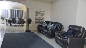 A modern living room with a black leather sofa, a dining area with a table and chairs, and a large artwork on the wall. - 3-bed Sea View House in Priory St Ann (St. Ann's Bay)