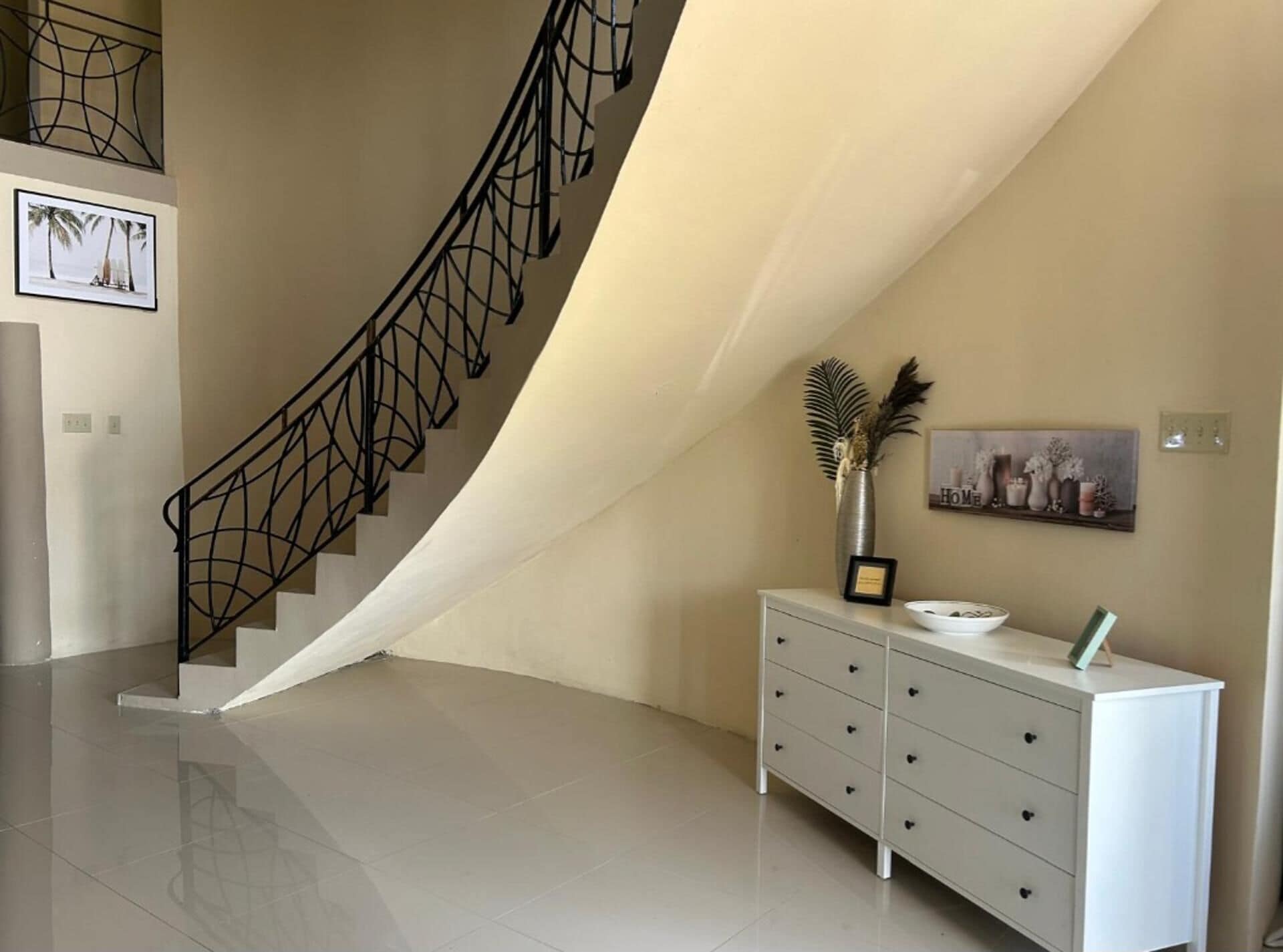 A modern interior with a curved staircase, a white dresser, and a framed artwork on the wall.