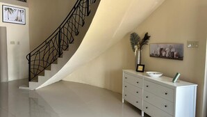 A modern interior with a curved staircase, a white dresser, and a framed artwork on the wall. - 3-bed Sea View House in Priory St Ann (St. Ann's Bay)