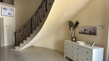 A modern interior with a curved staircase, a white dresser, and a framed artwork on the wall.