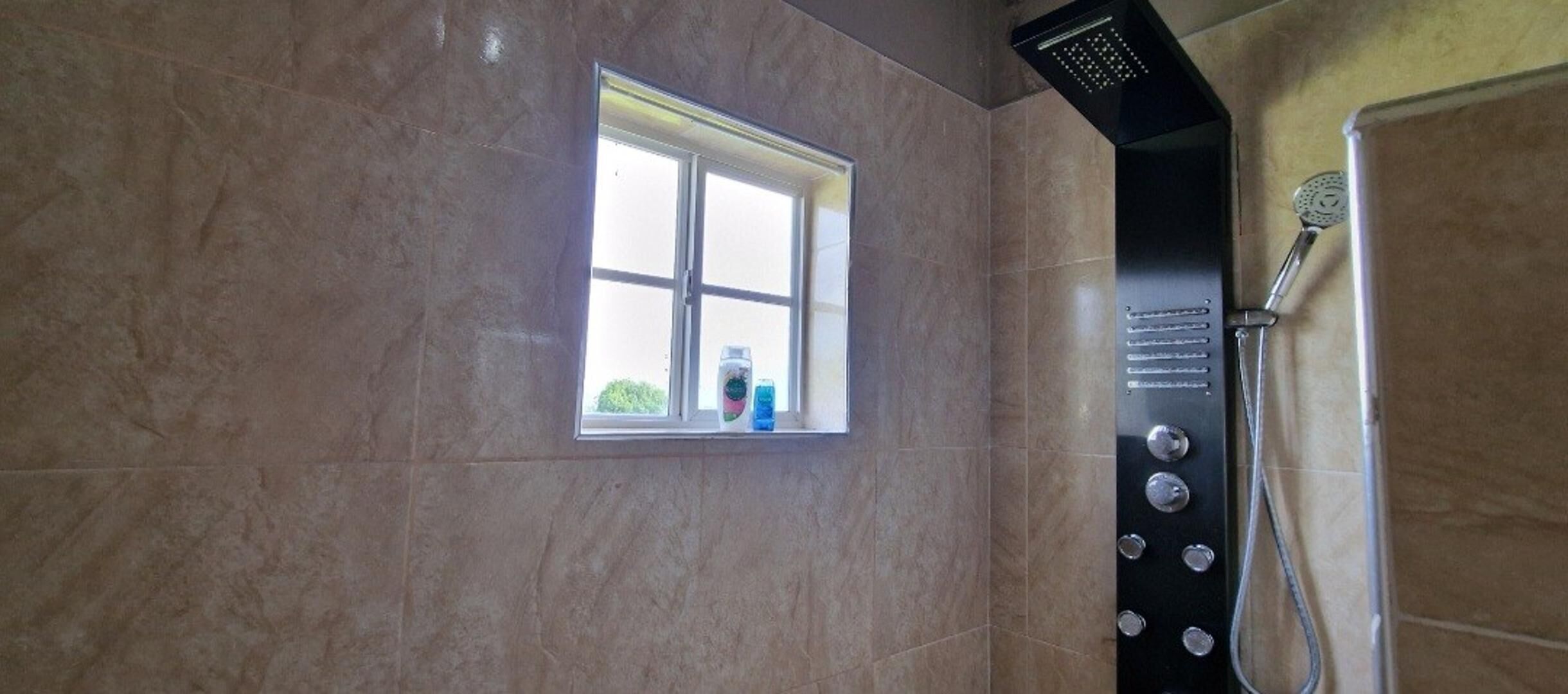 A bathroom with a window, a shower, and a wall-mounted control panel.