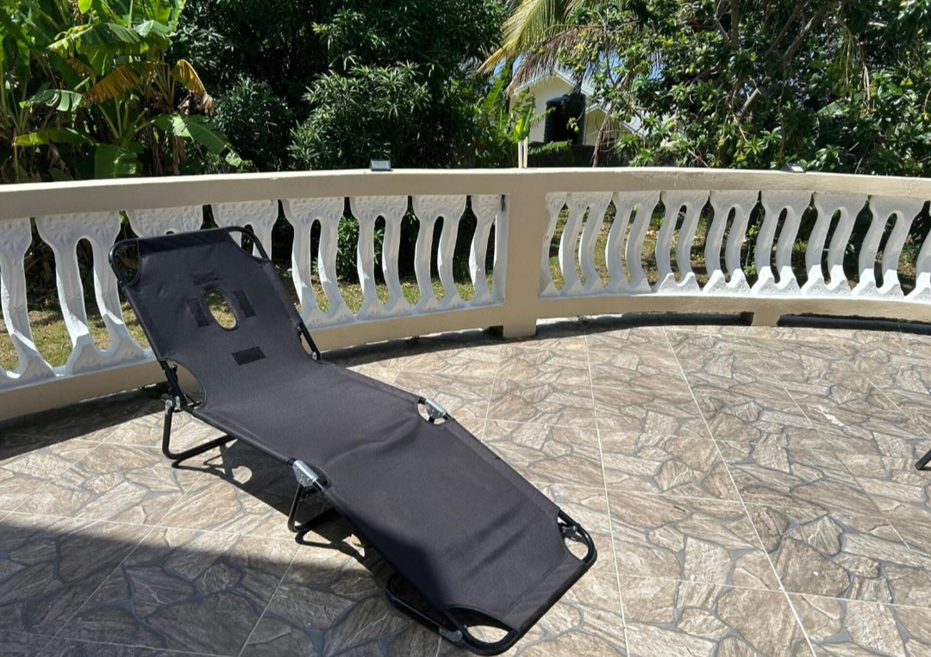 A sun lounger on a tiled patio with a white balustrade.