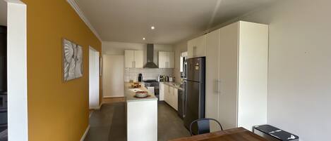 A modern kitchen with white cabinets, a central island, and a dining area with a wooden table and chairs.