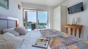 A hotel room with a bed, a TV, a desk, and a view of a pool and outdoor area. - Villa Rozeta with sea view (Šegotići)