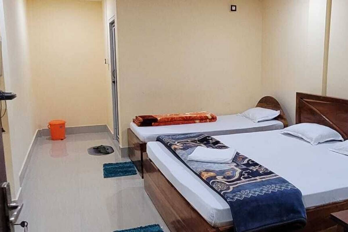 A hotel room with two beds, a wooden headboard, a small table with a bottle, and a trash bin.