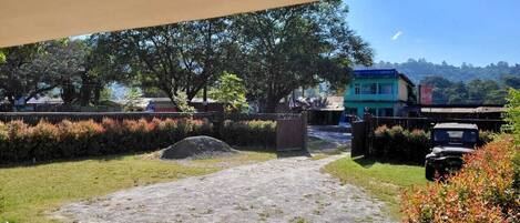 A paved pathway leading to a building with a blue roof, surrounded by greenery and a parked vehicle.