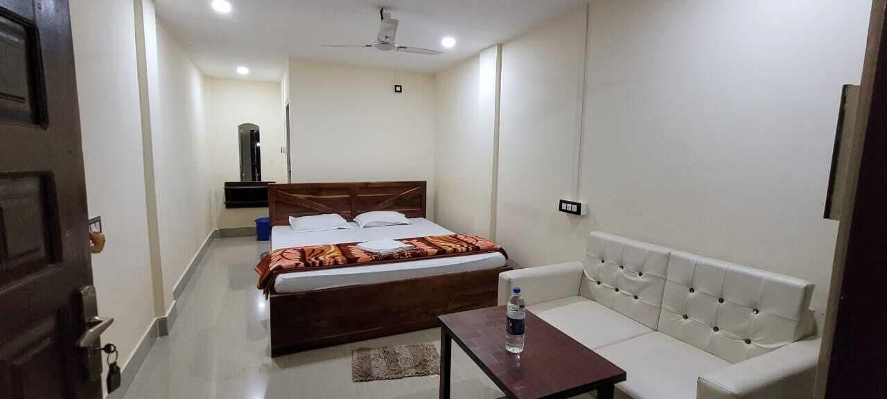 A hotel room with a bed, a sofa, a small table, and a ceiling fan.