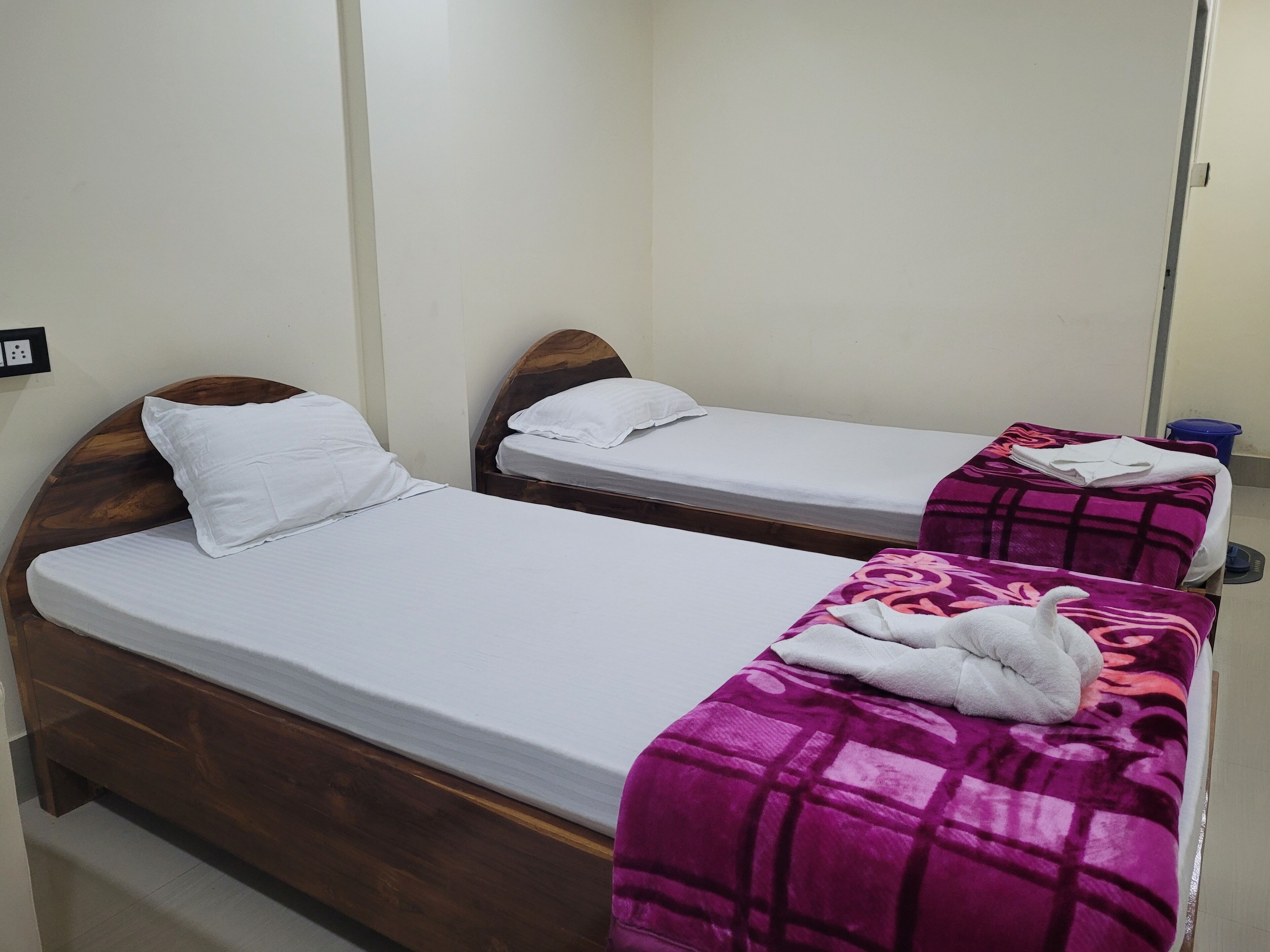 Dos camas individuales con cabeceros de madera, ropa de cama blanca y una manta morada sobre una de ellas.