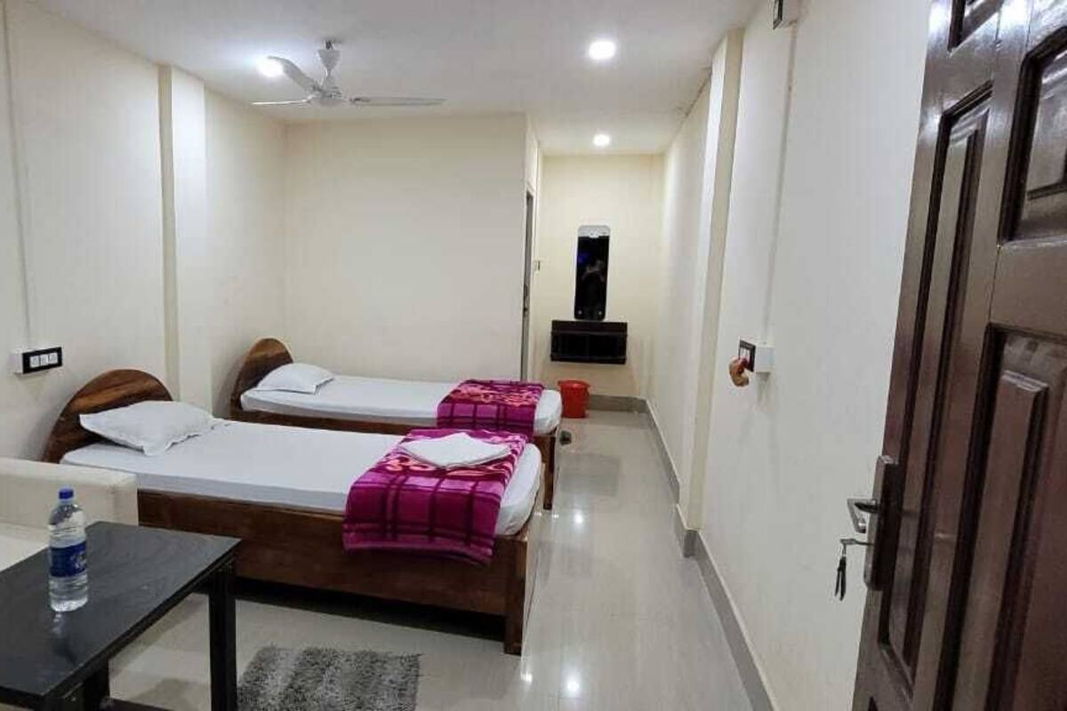 A hotel room with two single beds, a sofa, a small table, and a ceiling fan.
