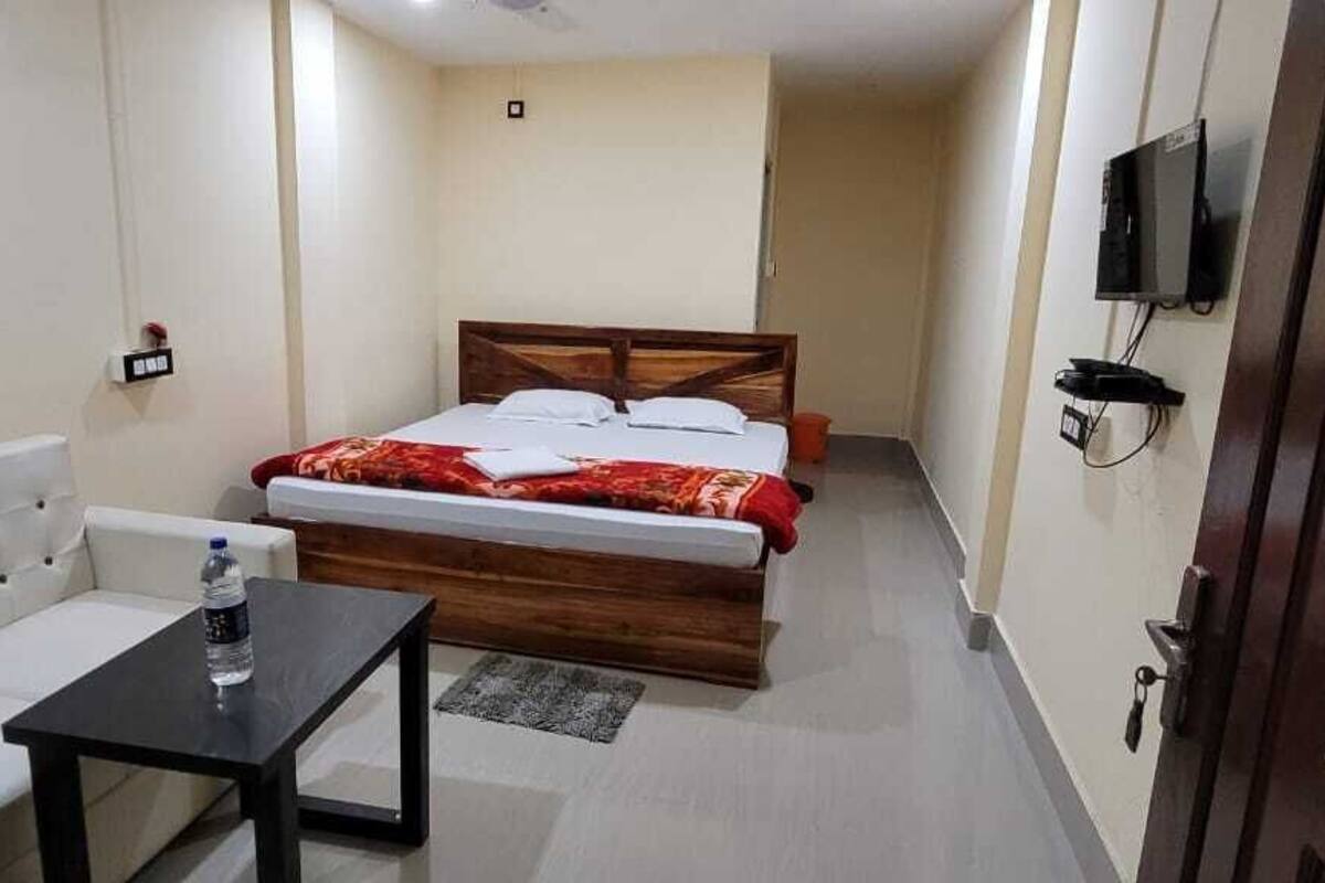 A small, compact room with a bed, a sofa, a small table, and a TV mounted on the wall.
