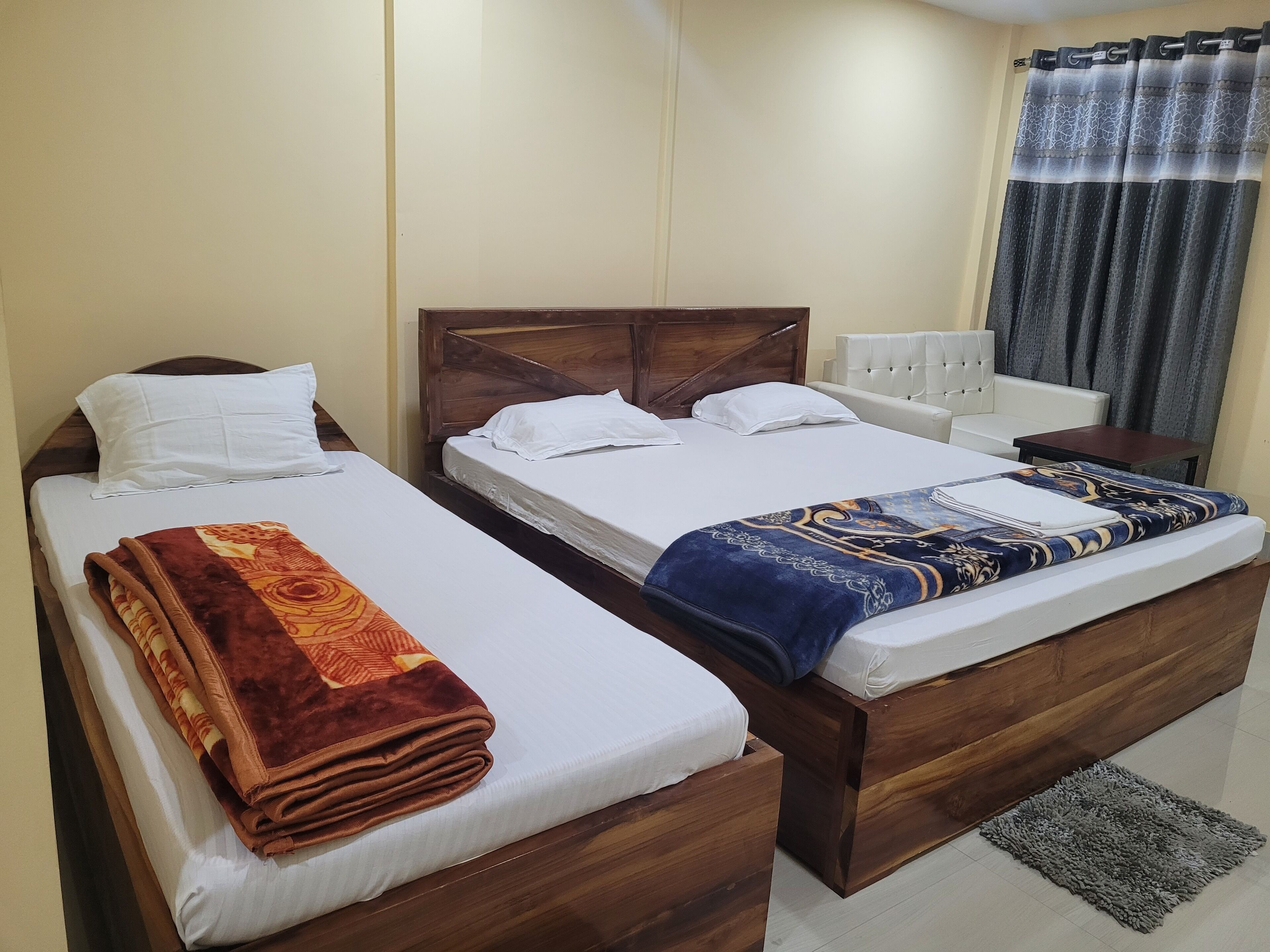 A hotel room with two wooden beds, white linens, and a patterned blanket on one bed.