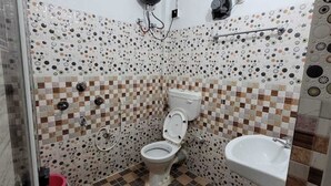Et badeværelse med flisegulv, toilet, vask og bruseområde.