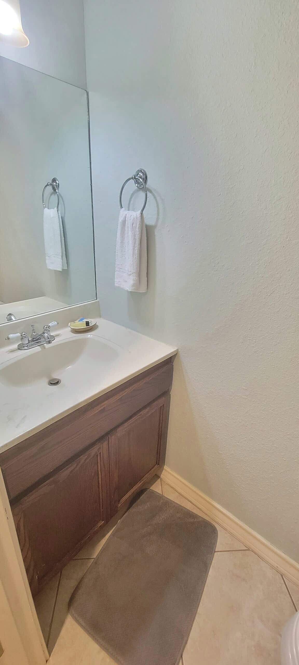 Un baño con lavamanos, espejo y dos toallas colgadas en aros.
