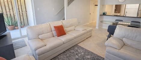Ein Wohnzimmer mit einer Couch, einem Couchtisch, einem Fernseher und einem Essbereich mit Tisch und Stühlen.