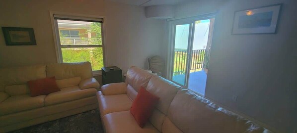 A living room with two sofas, a small table, and a sliding glass door leading to a balcony.