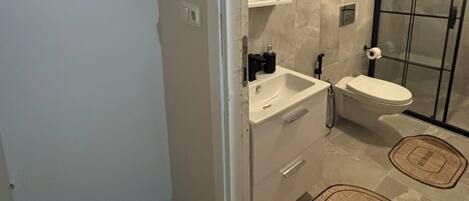 A modern bathroom with a glass shower enclosure, a white sink, and a toilet. There are two bathroom rugs on the floor.