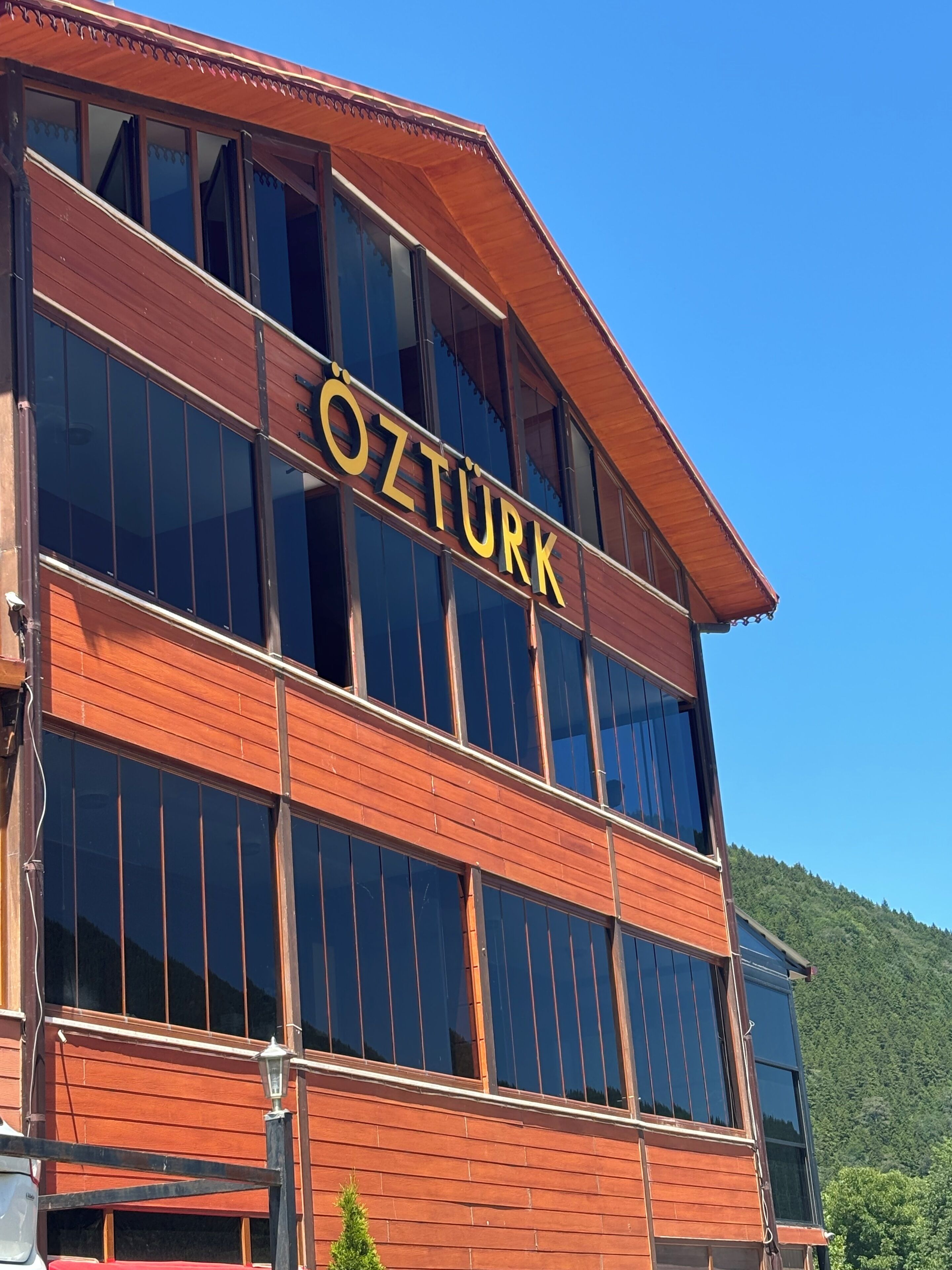 A building with the sign "ÖZTÜRK" on the facade, large windows, and a wooden exterior.