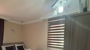 A hotel room with a bed, a small table with a plant, a radiator, and a window with blinds. - Uzungöl Ozturk Hotel  (Çaykara)